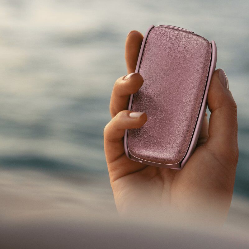 Ruka držící Ploom X Advanced růžové zařízení se zadním koženým krytem
